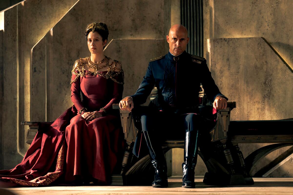 A couple in regal dress sitting on thrones.