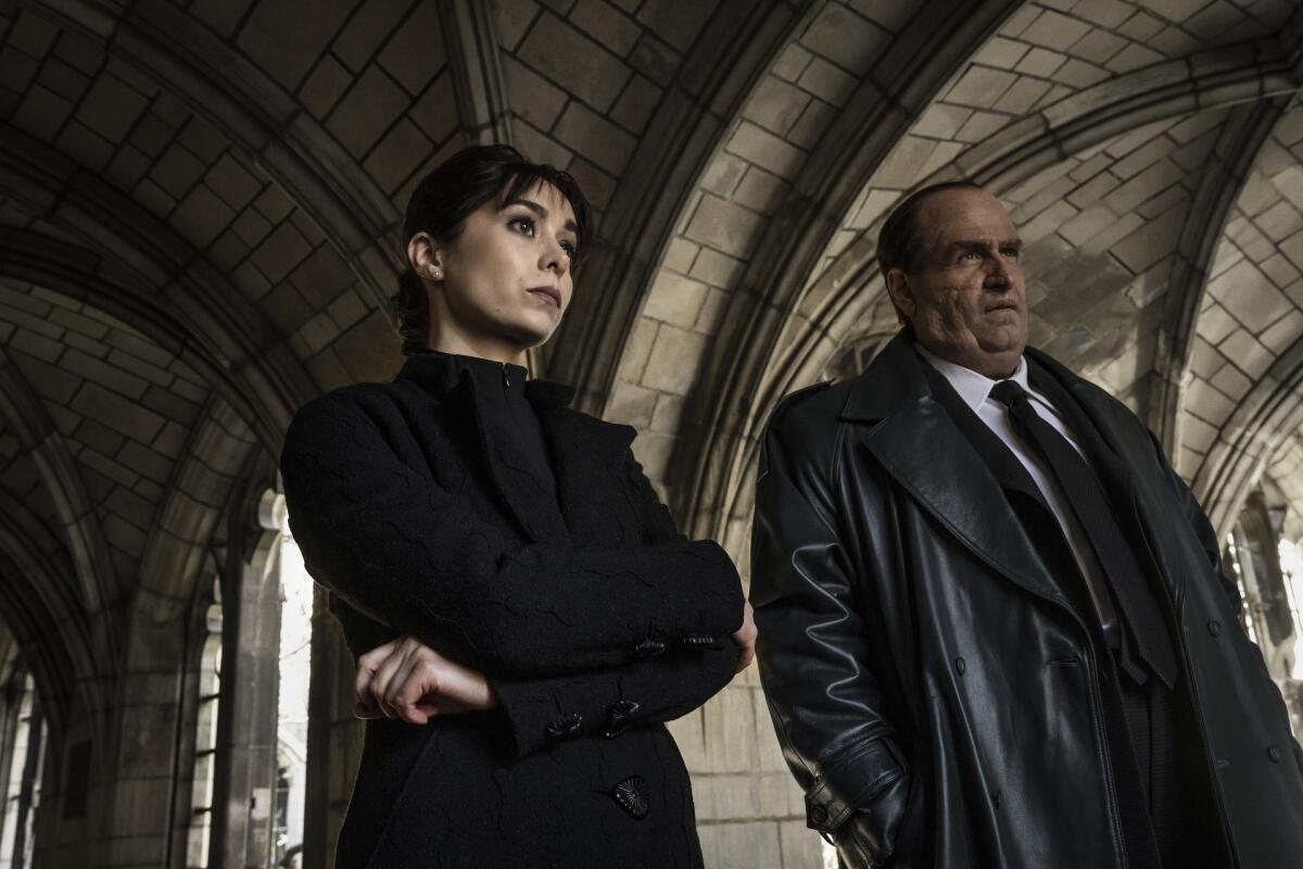 A woman and a man both wearing black stand under a stone arched roof.