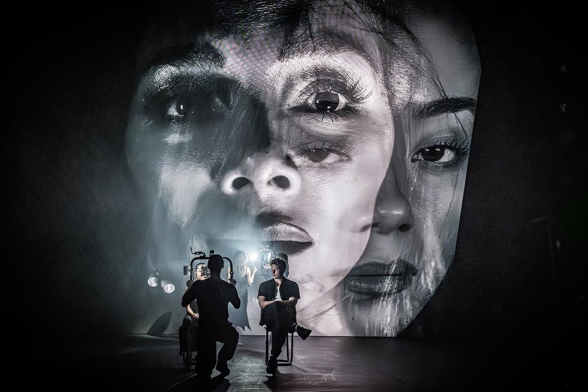 Two people seated onstage in front of a projection of two large women's faces