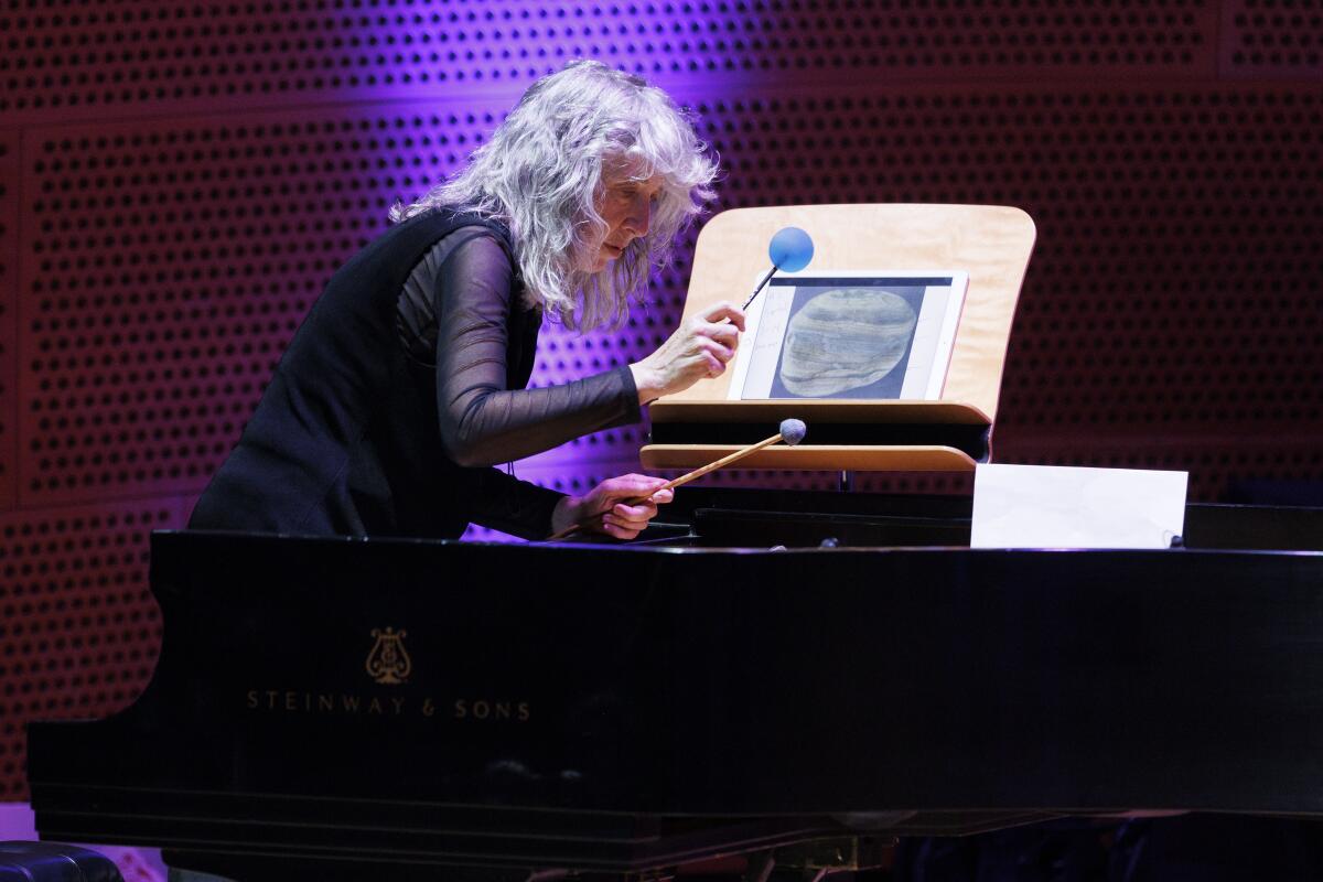 A woman in all black is spotlighted as she plays percussion.