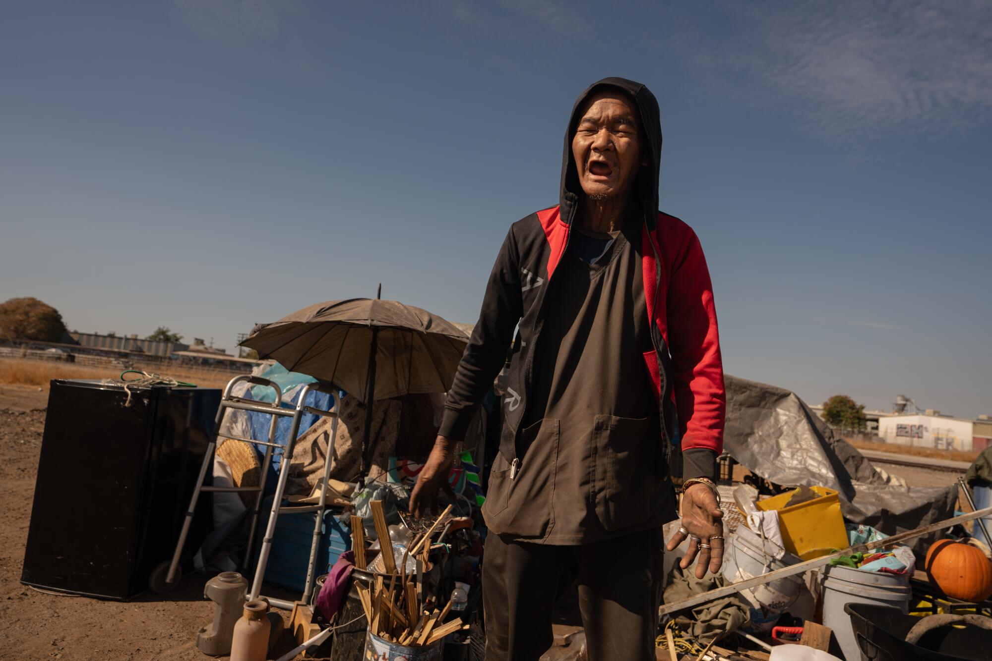 Oudom Thammavong stands with his possessions at a homeless encampment in Fresno. 