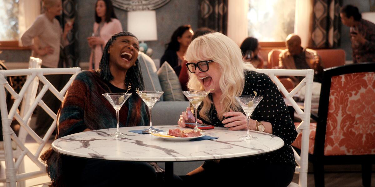 Two older women laughing and sitting at a table with four martini glasses.