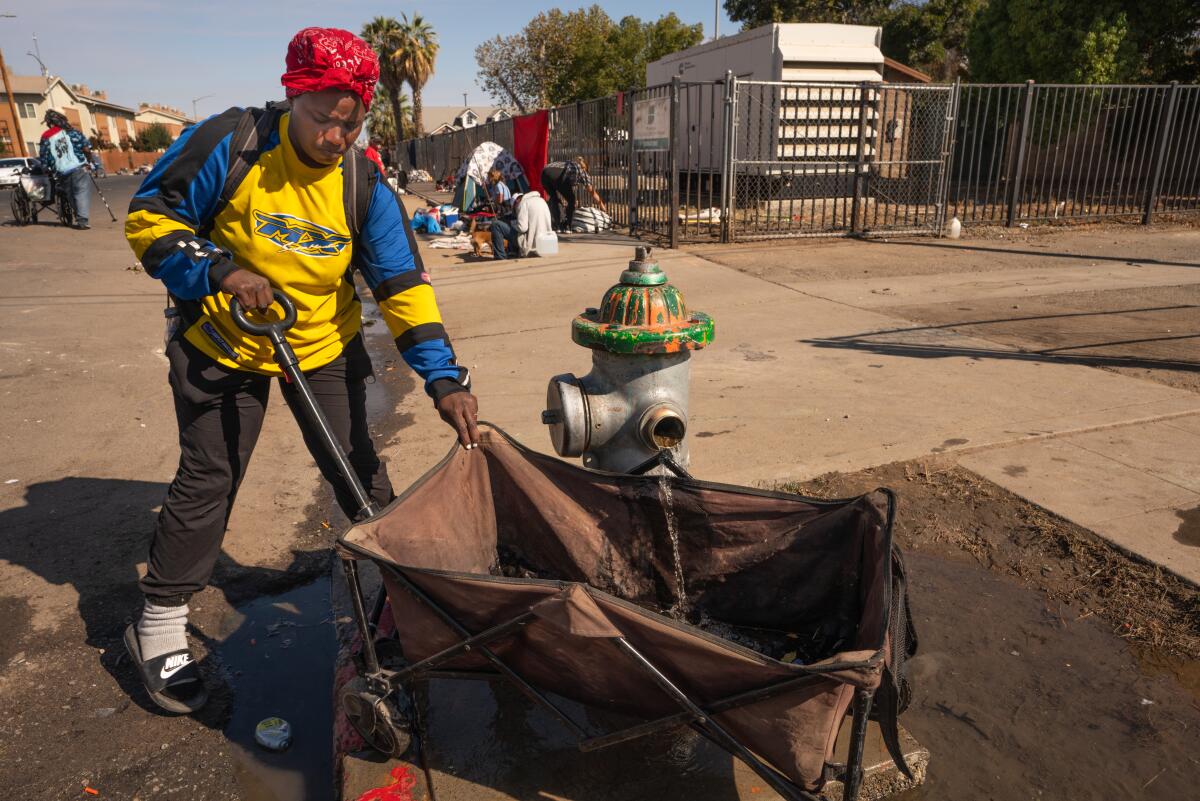 An unhoused woman gets water from a hydrant before the demolition of homeless encampment on Santa Clara Street in Fresno.