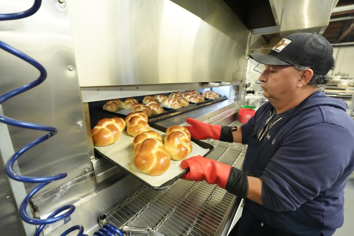 A man lifts a tray of bread from an oven. 