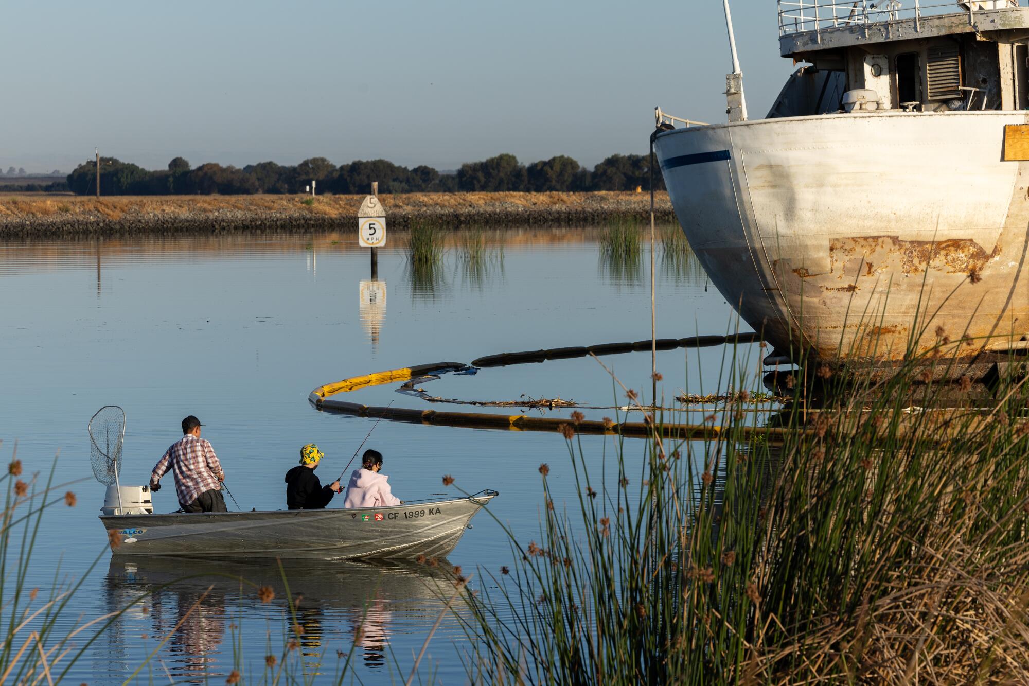 Fishermen cast lines outside an oil boom surrounding the battered Aurora.