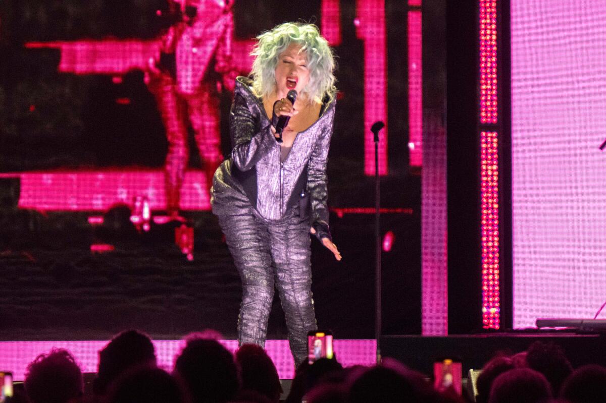 Cyndi Lauper performs on a pink-lit stage.