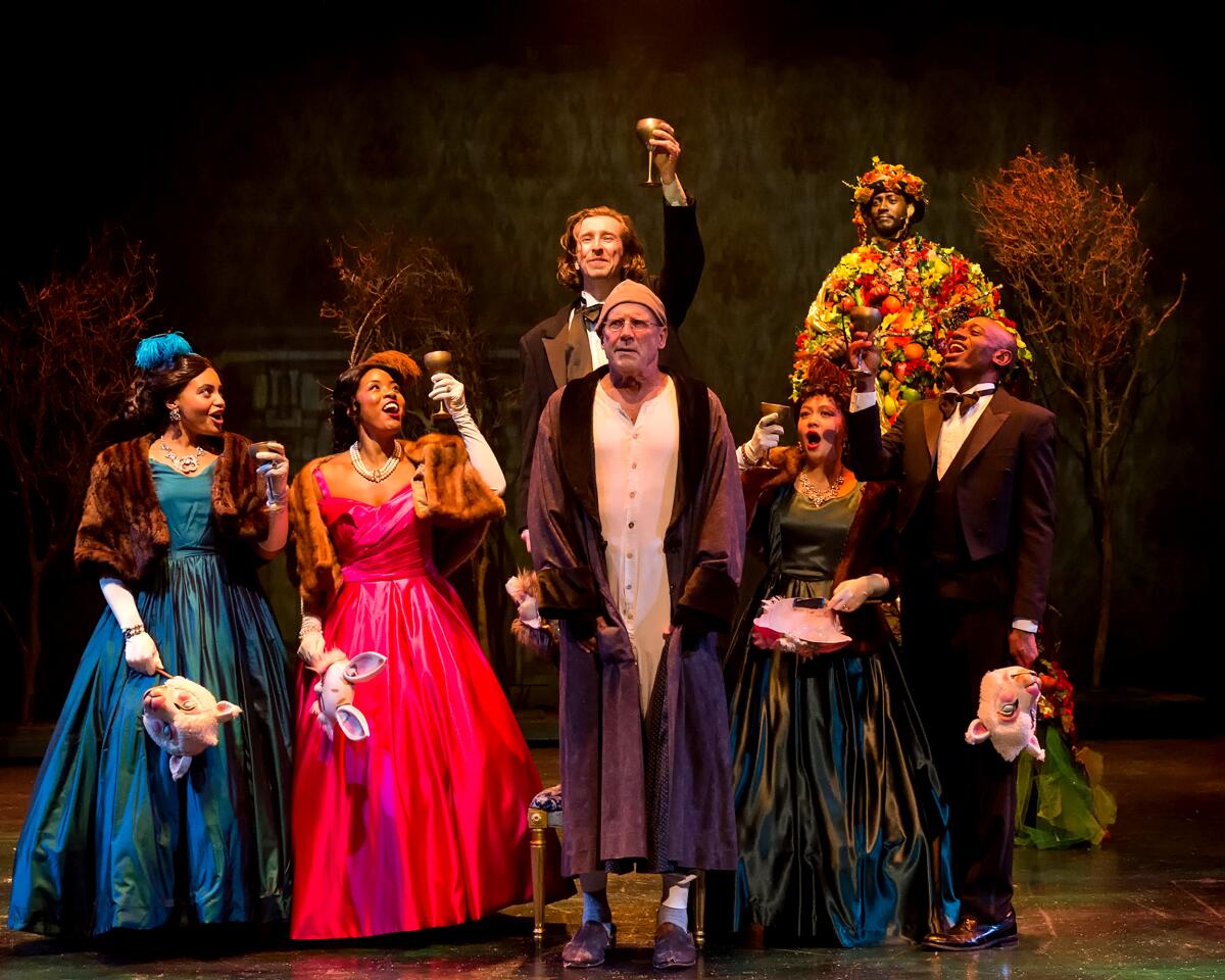 Actors in Victorian fancy dress around a man in a dressing gown in "A Christmas Carol"