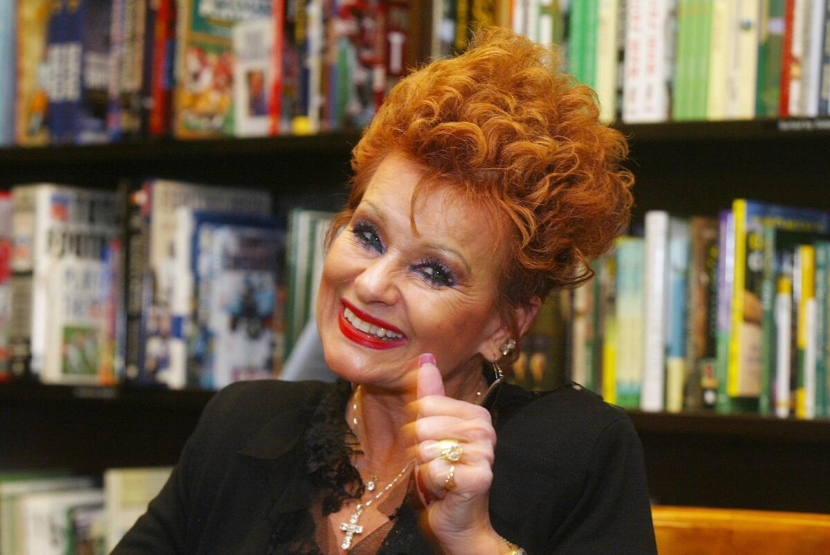 Tammy Faye Messner gives a thumbs-up in front of a shelf filled with books