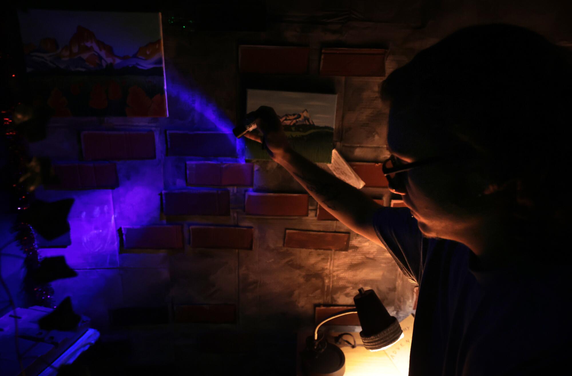 UCLA student Tyler Neufeld shines a blacklight on a wall to reveal a handprint. 