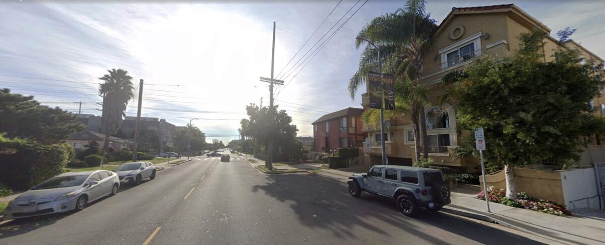 A street with a large building and a smaller building on it and cars parked along it.