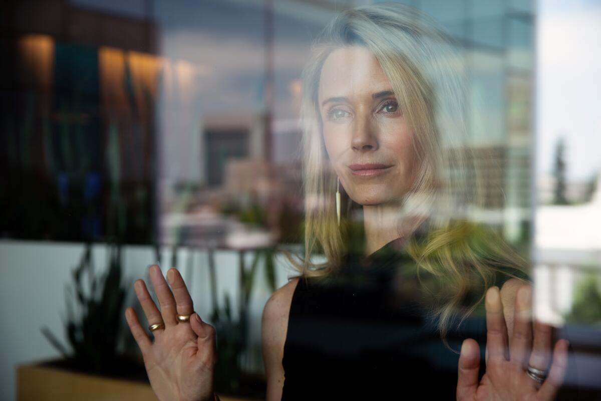 Jennifer Siebel Newsom seen looking through a vertical glass surface from the other side as she rests both hands on it