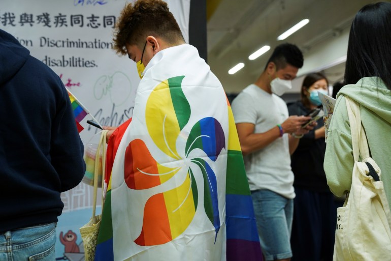 A supporter of LGBT rights covered with rainbow flag of Hong Kong checks his phone at the Rainbow Market since the annual pride parade was cancelled for the last two years due to the outbreak of COVID-19 in Hong Kong, China, November 13, 2021. REUTERS/Lam Yik