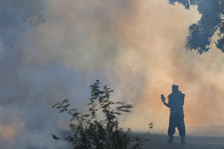 A supporter of the former Pakistani Prime Minister Imran Khan's party, Pakistan Tehreek-e-Insaf (PTI), holds a mobile phone amid tear gas smoke as he attends an anti-government protest demanding the release of Khan, in Islamabad, Pakistan, November 26, 2024. REUTERS/Akhtar Soomro