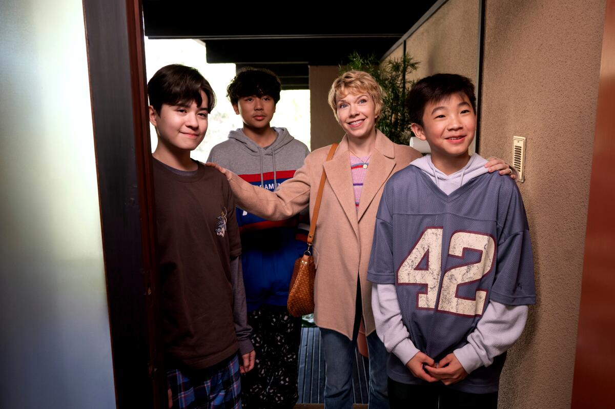 Three boys with their mother stand in a doorway smiling.