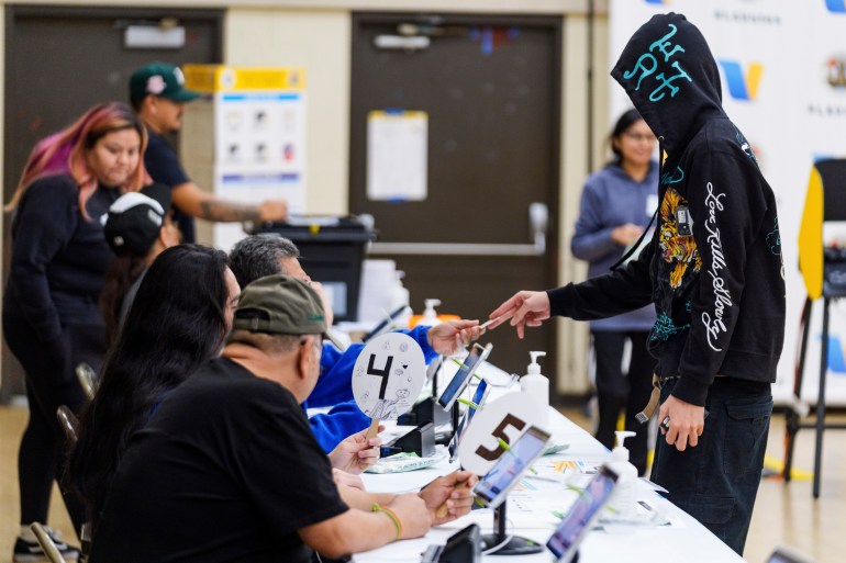 A man in a hoodie walks up to a panel of election worker sitting at a long table to vote.