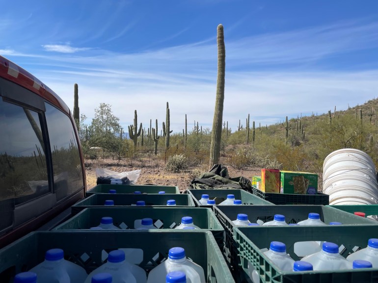 The back of a truck is filled with water jugs, in the Sonoran Desert