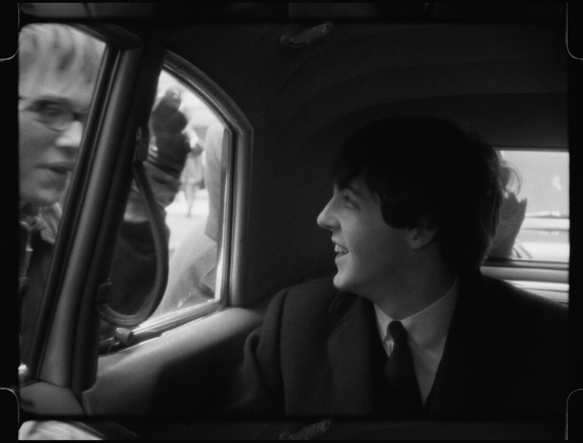 A man sitting in a car looking out the window as people tap on the door.