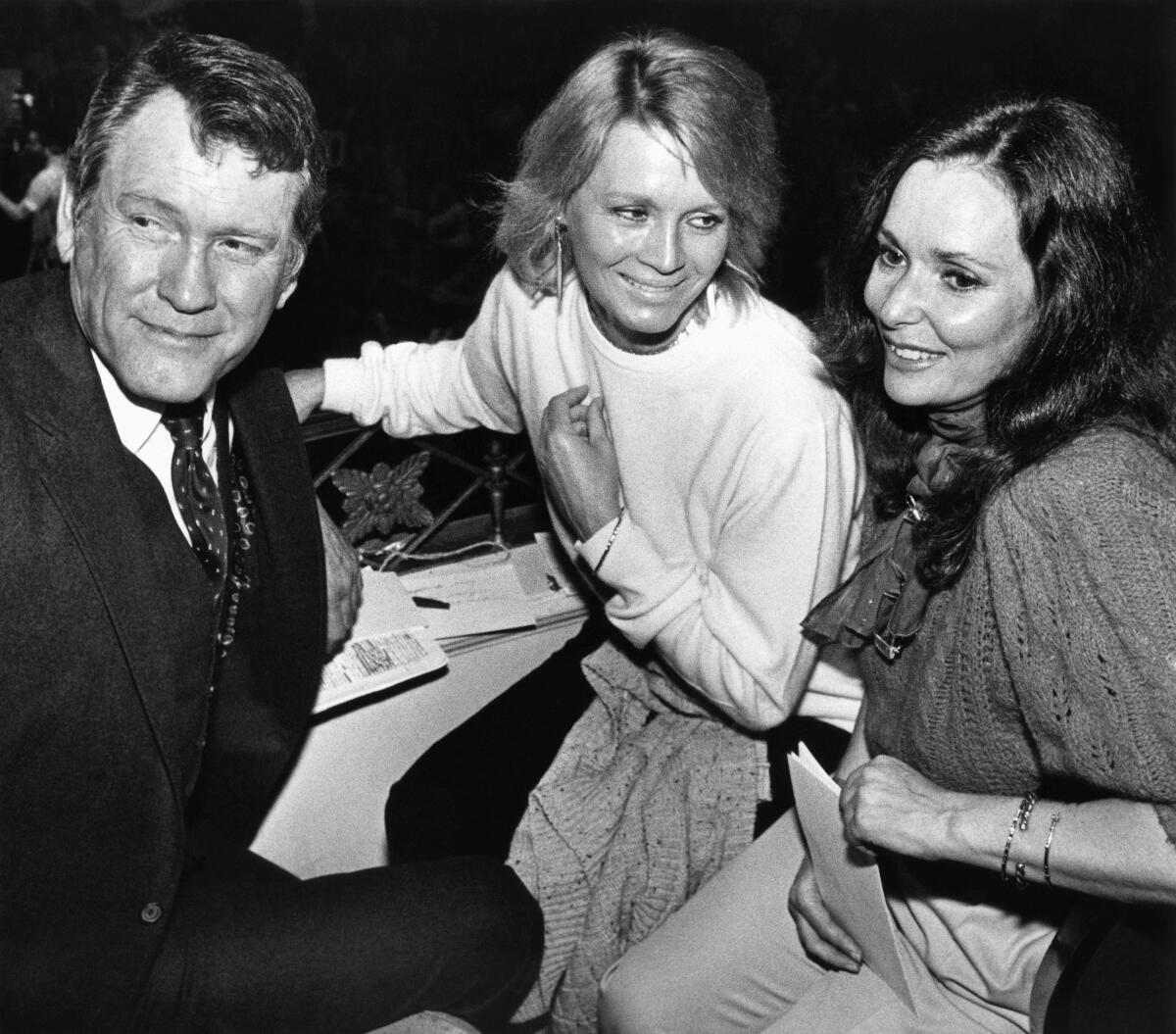 A man and two women sit together at a hotel table in a black-and-white photo