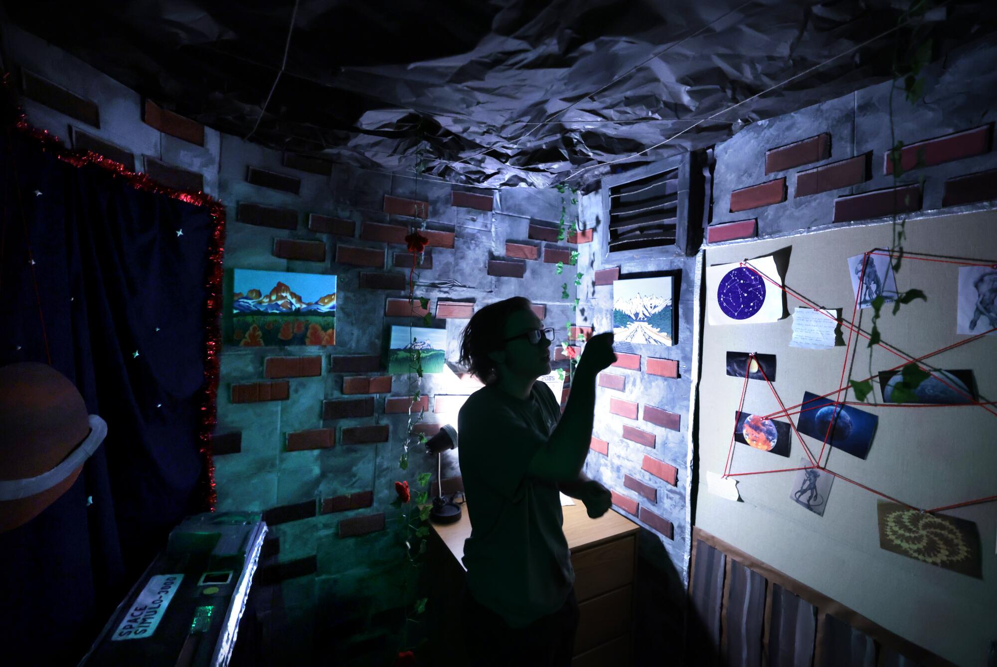 UCLA student Tyler Neufeld shines a flashlight on a corkboard filled with puzzles. 