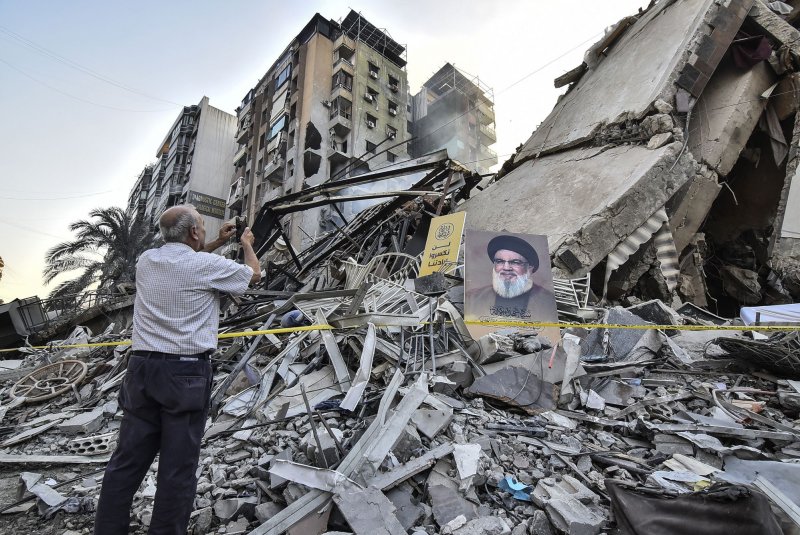 A man takes a picture of a portrait of slain Hezbollah chief Hassan Nasrallah in front of the rubble of a building at the site of an Israeli airstrike in Beirut's southern suburbs on Thursday. Waves of IDF airstrikes targeting Hezbollah were launched against the area again on Saturday. Photo by Fadel Itani/UPI