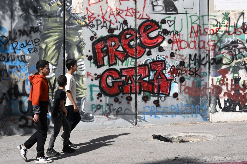 Palestinian youth walk past graffiti reading Free Gaza on the Israeli separation wall in Bethlehem, West Bank, on Friday. Photo by Debbie Hill/ UPI