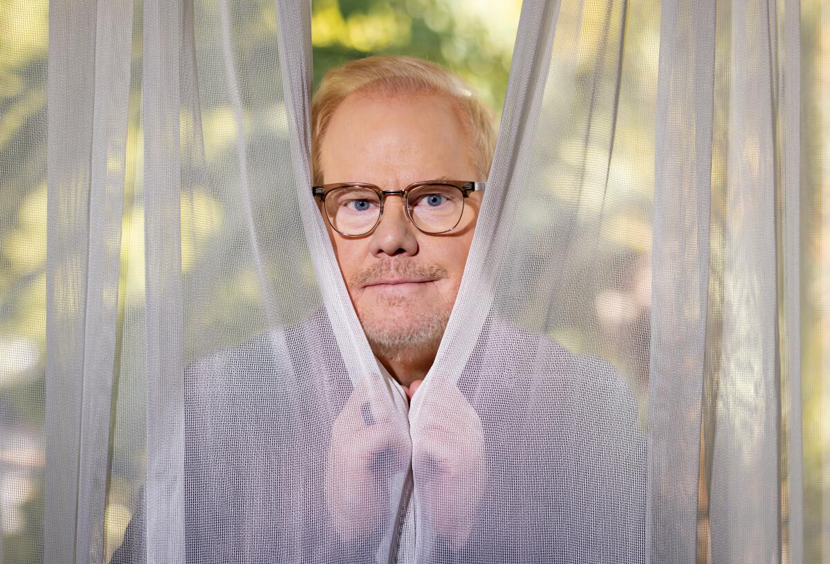 Man in glasses peaking between sheer curtains