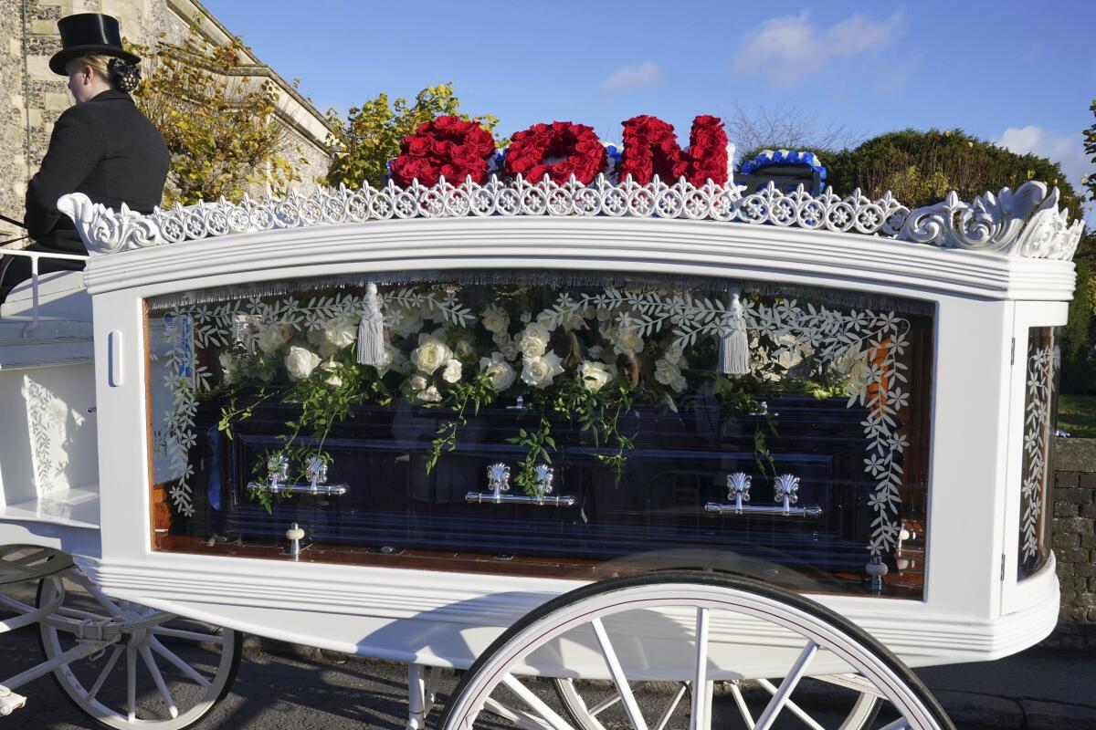 A see-through horse-drawn carriage with "son" on top in red flowers carries the coffin of Liam Payne draped in white flowers