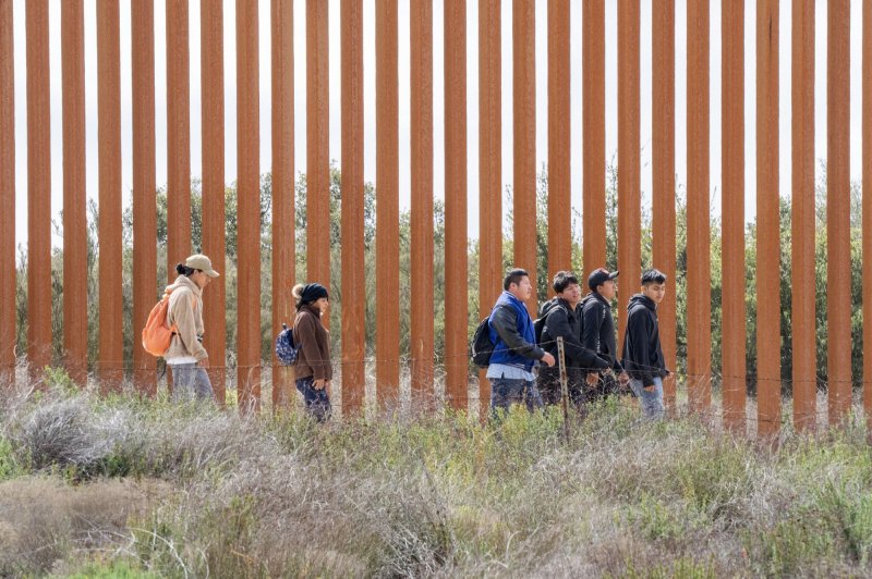 Migrants walk along the United States side of the border wall with Mexico to surrender to the U.S. Border Patrol near Campo, California in March. File photo by Pat Benic/UPI