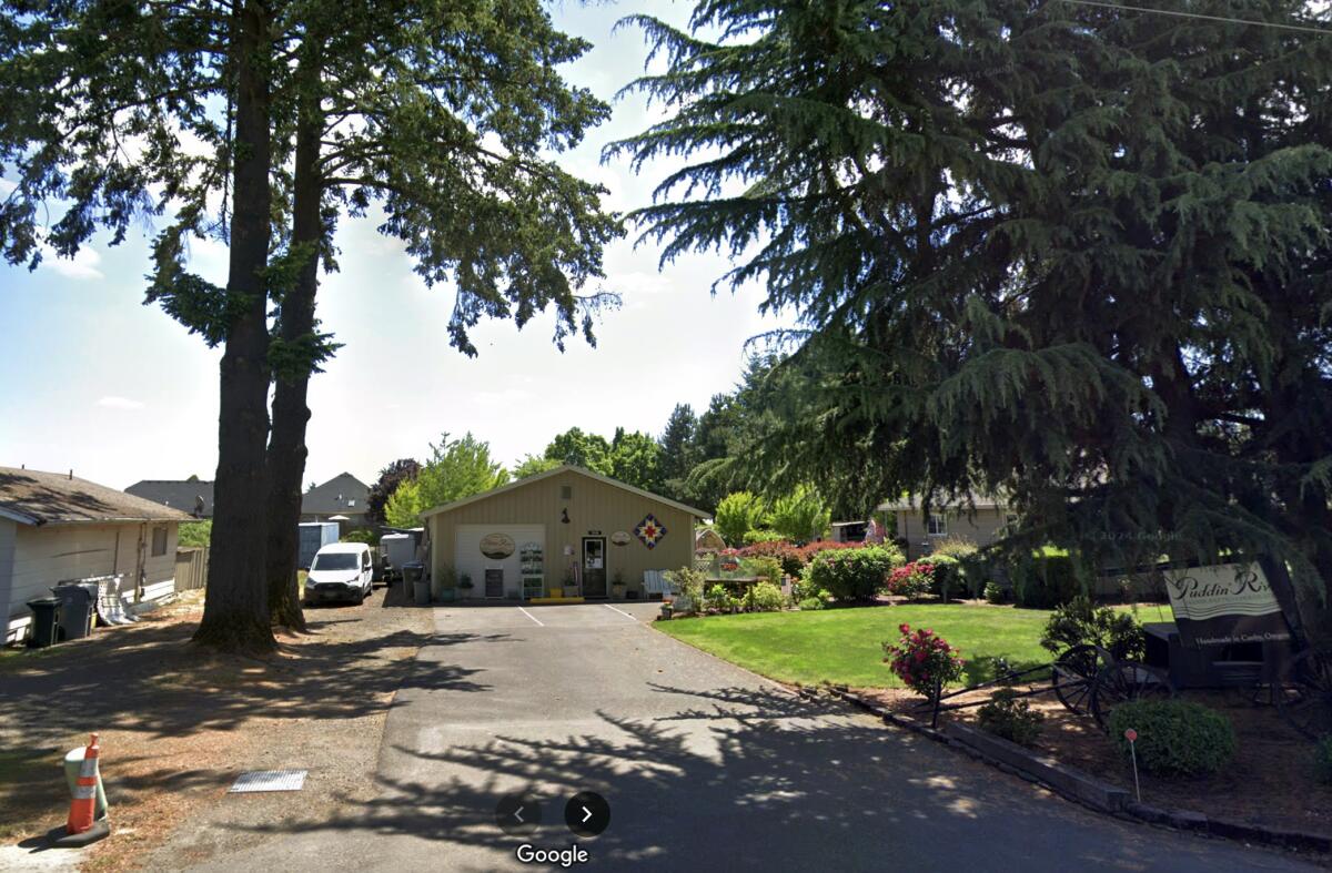 A building and van at the end of a driveway, with a lawn, evergreens and a sign reading "Puddin' River" in the foreground