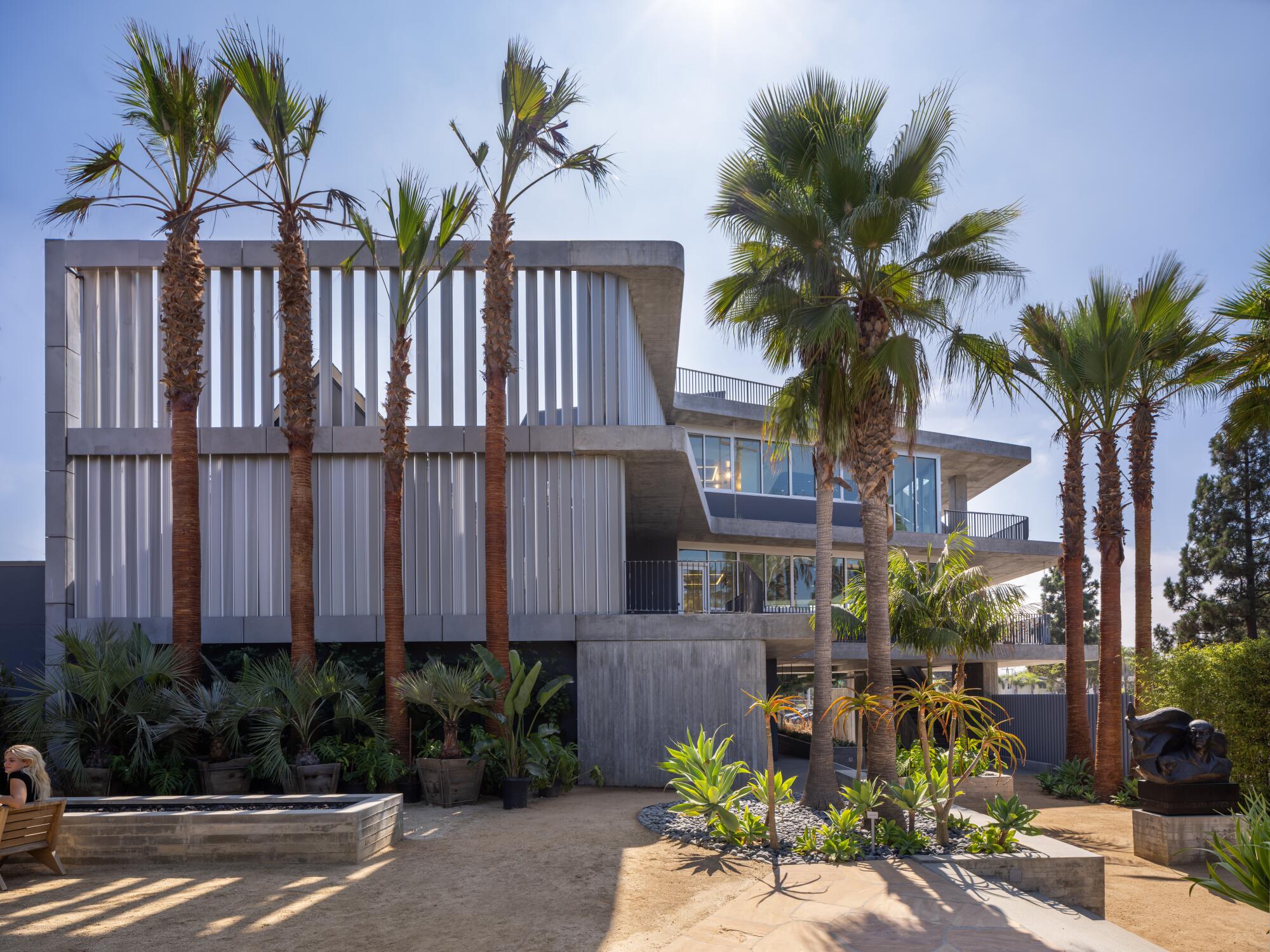 Vertical louvers and abundant windows soften the exterior appearance of a gray concrete building.