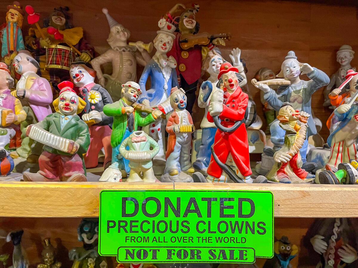 Several clown miniatures sit on a shelf; a sign reads "Donated precious clowns from all over the world."