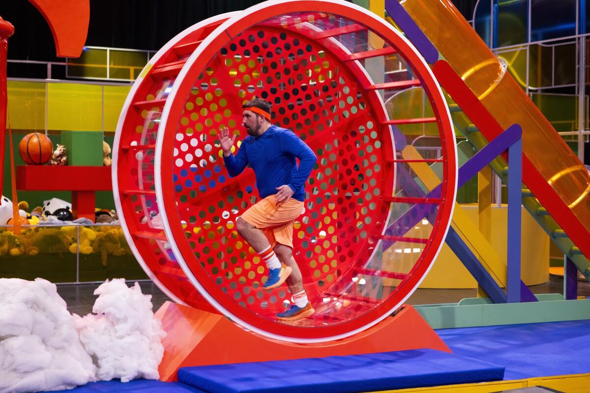 A man in athletic apparel runs in a human-scale hamster wheel.