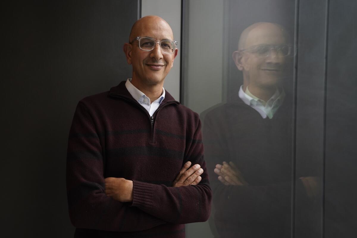 Dr. Mark Ghaly smiling for a portrait beside his reflection in a window