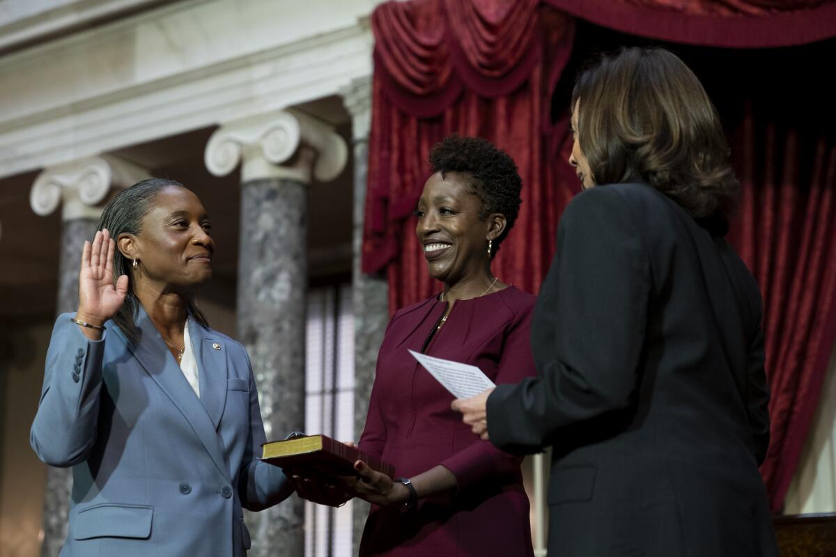 Laphonza Butler stands facing Kamala Harris with her right hand raised and her left hand on a Bible held by Neneki Lee.