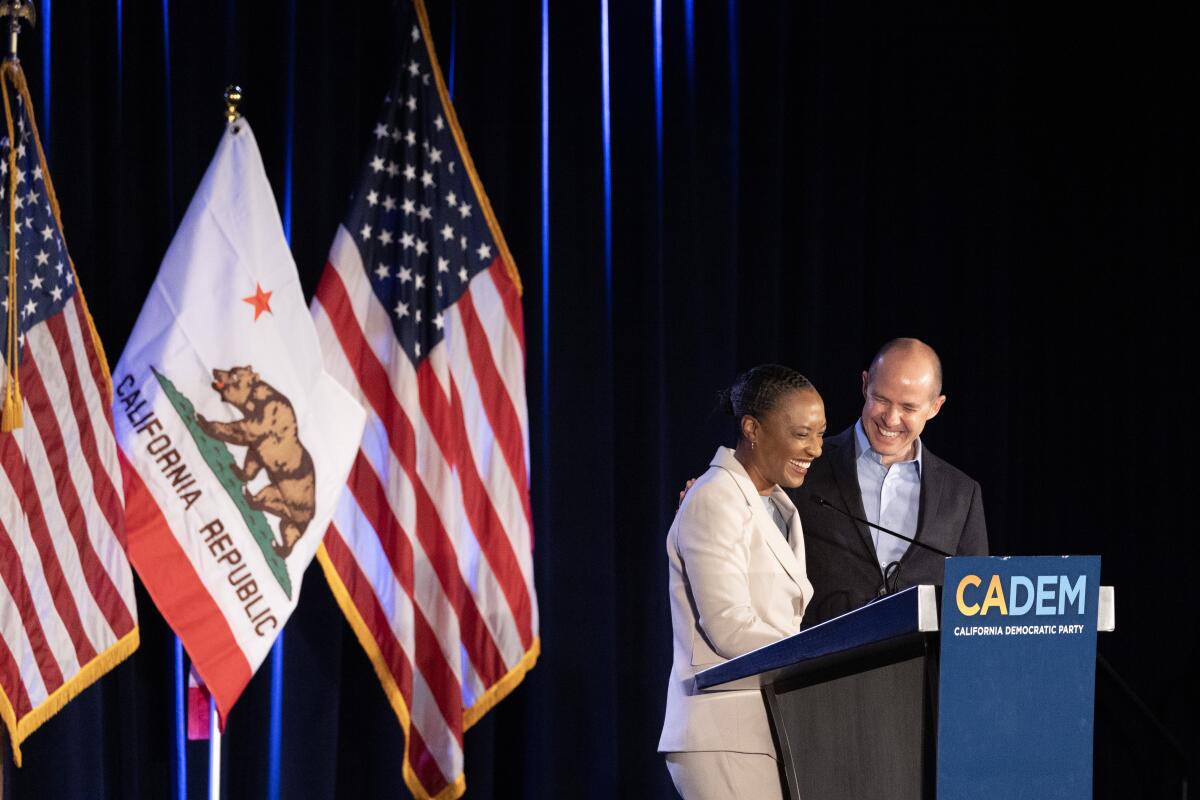 Laphonza Butler and Rusty Hicks standing at a lectern alongside American and California flags.