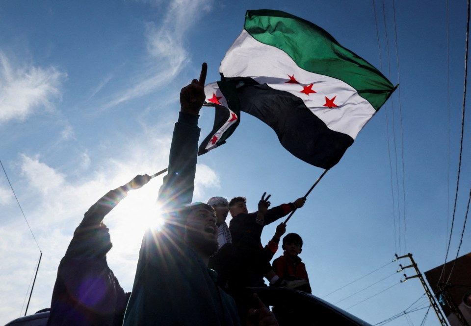 A person waves a Syrian opposition flag as people celebrate at Masnaa Border Crossing, after Syrian rebels announced that they have ousted President Bashar al-Assad on December 8, 2024