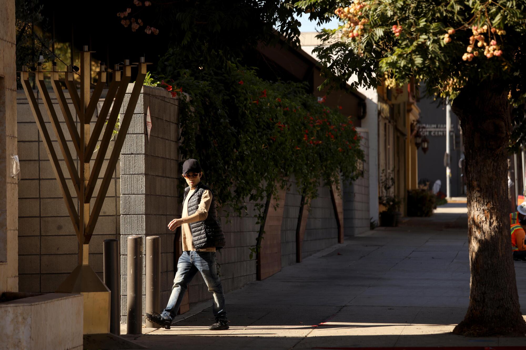 A man walks past a menorah on a sidewalk.