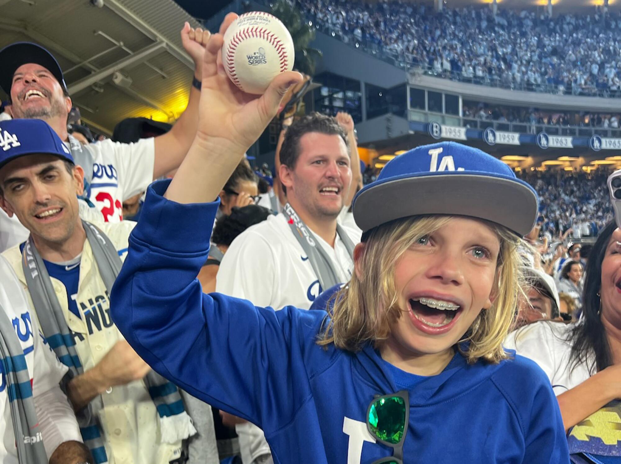 Zachary Ruderman holds up a baseball and smiles in the stands.