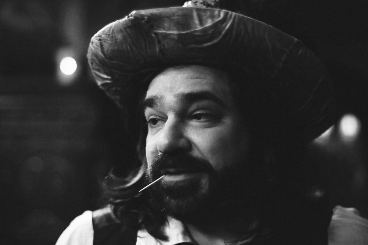 A black and white photo of a man wearing a hat with toothpick in his mouth.