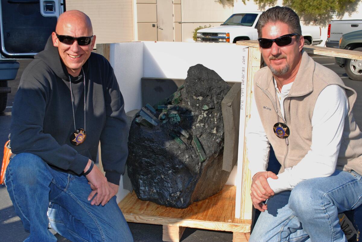 Two men kneel, with a black bag between them.