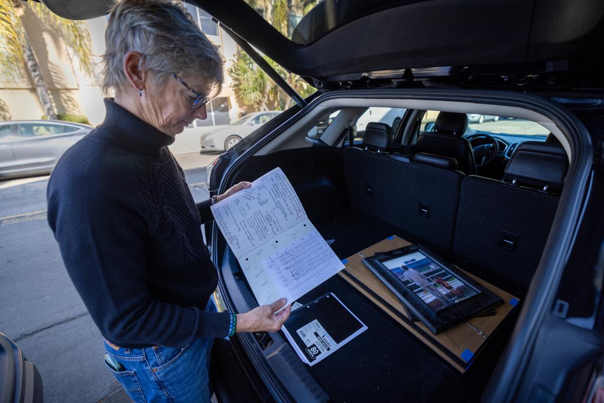 A woman looks at a notebook behind the back of a vehicle.