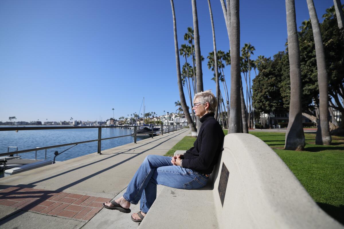 A woman sits on a bench and looks out over a body of water.