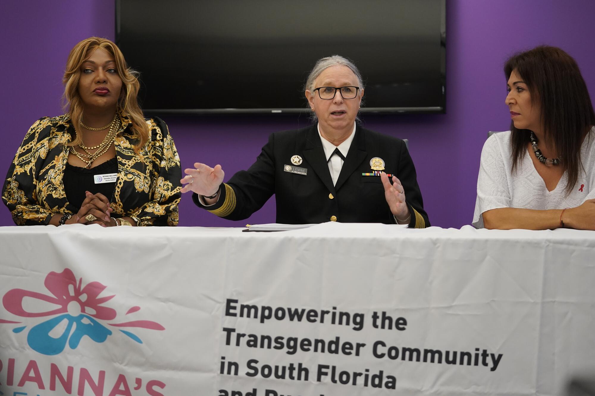 Three women behind a table draped with an "Empowering the Transgender Community in South Florida" banner 