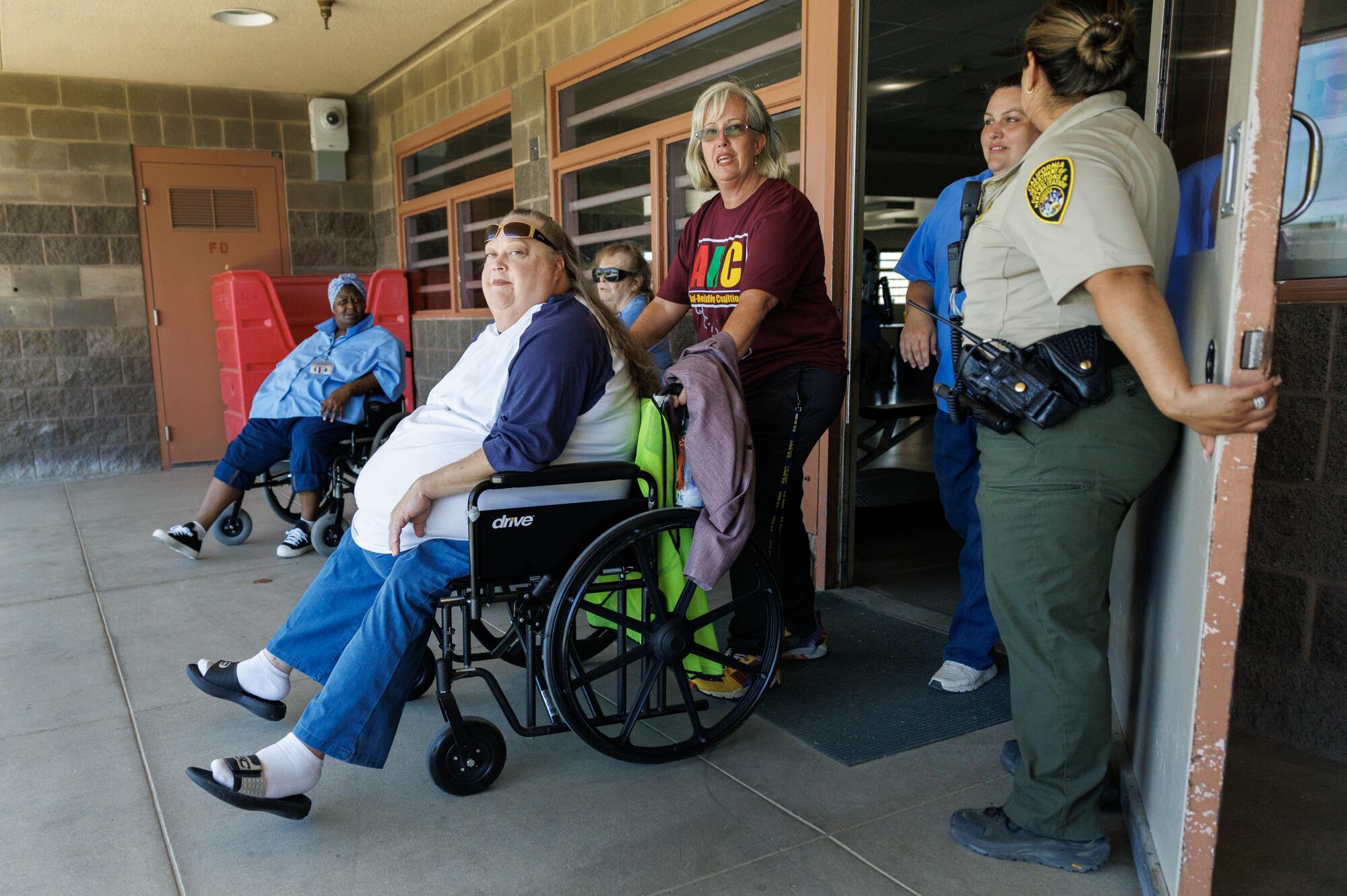 A guard opens a door near women who are in wheelchairs or standing.