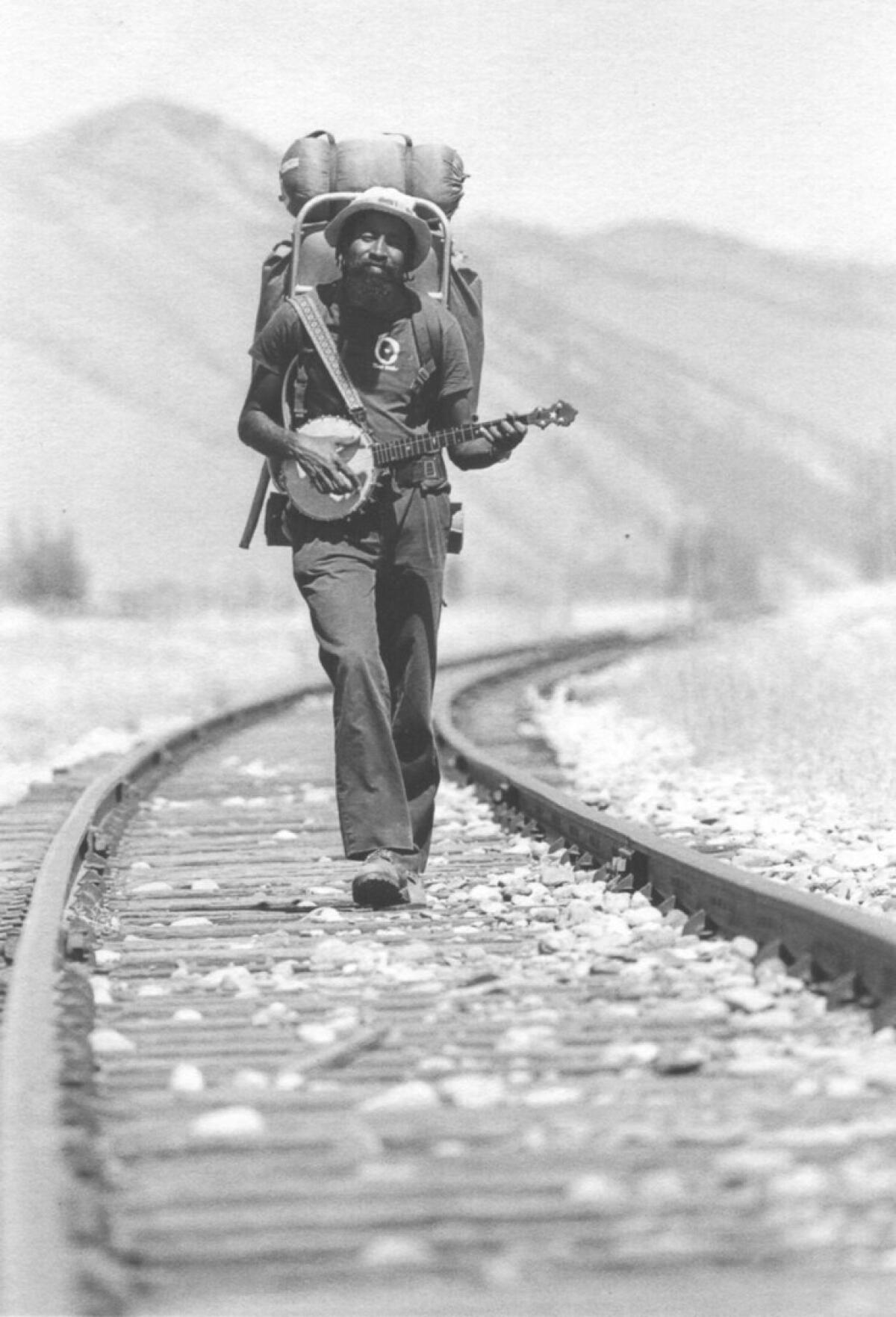 John Francis walks on train tracks in a black-and-white photo 