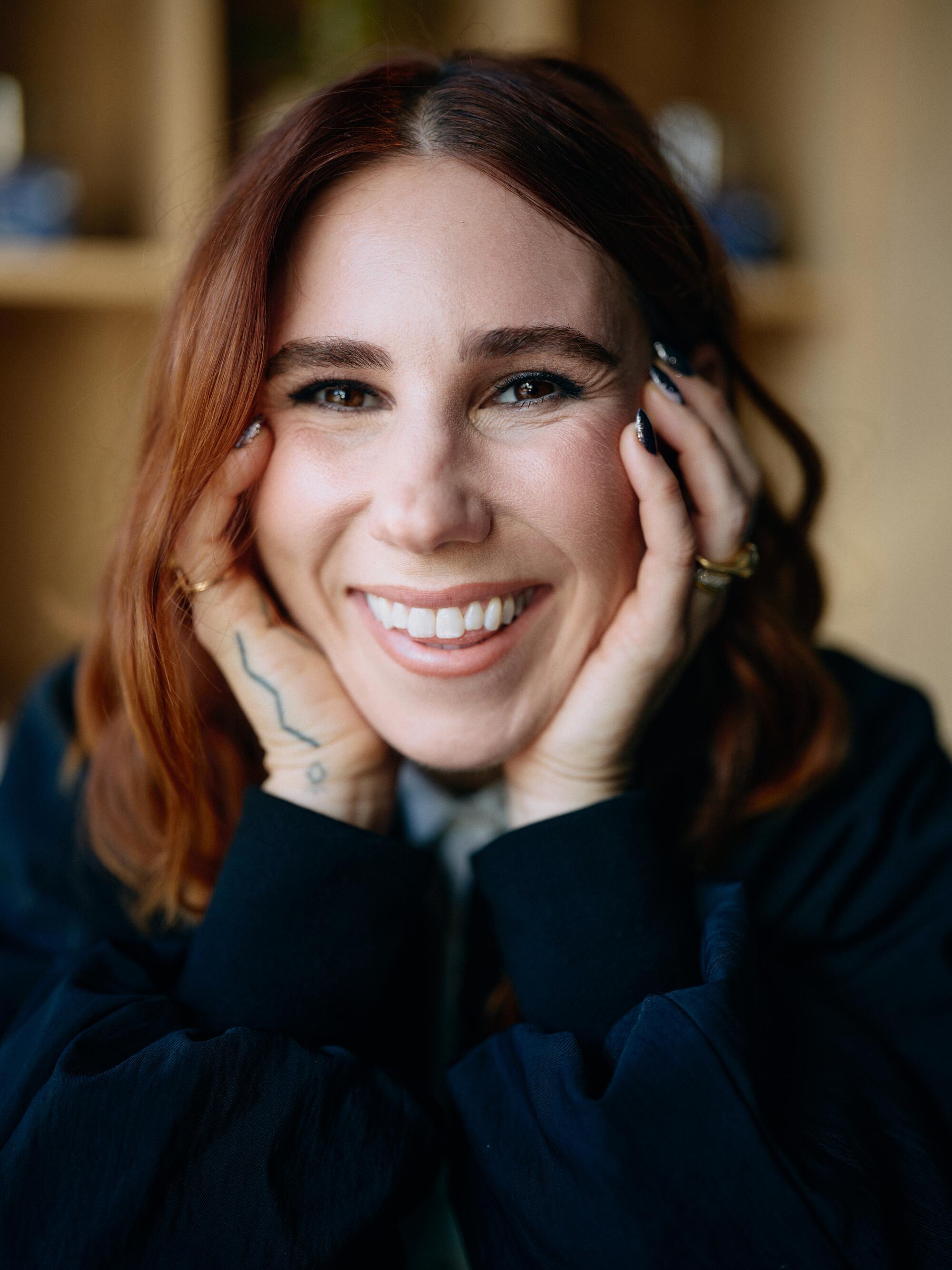 A closeup of a woman with red hair holding her hands on the side of her face.