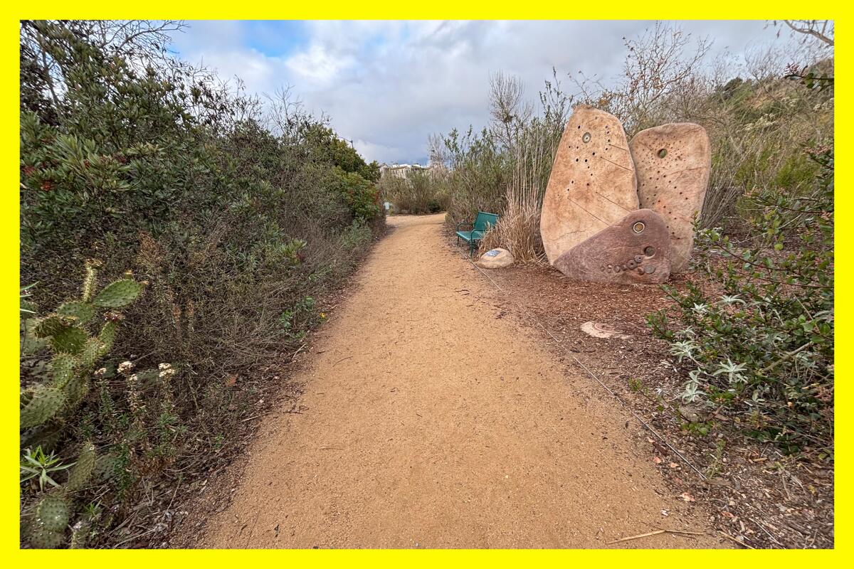 A narrow dirt path passes by a rock formation which honors the Tongva people.