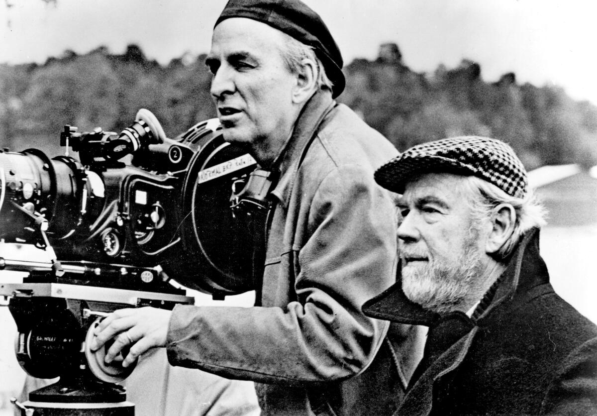 A director and a cinematographer line up a shot while standing at a camera.