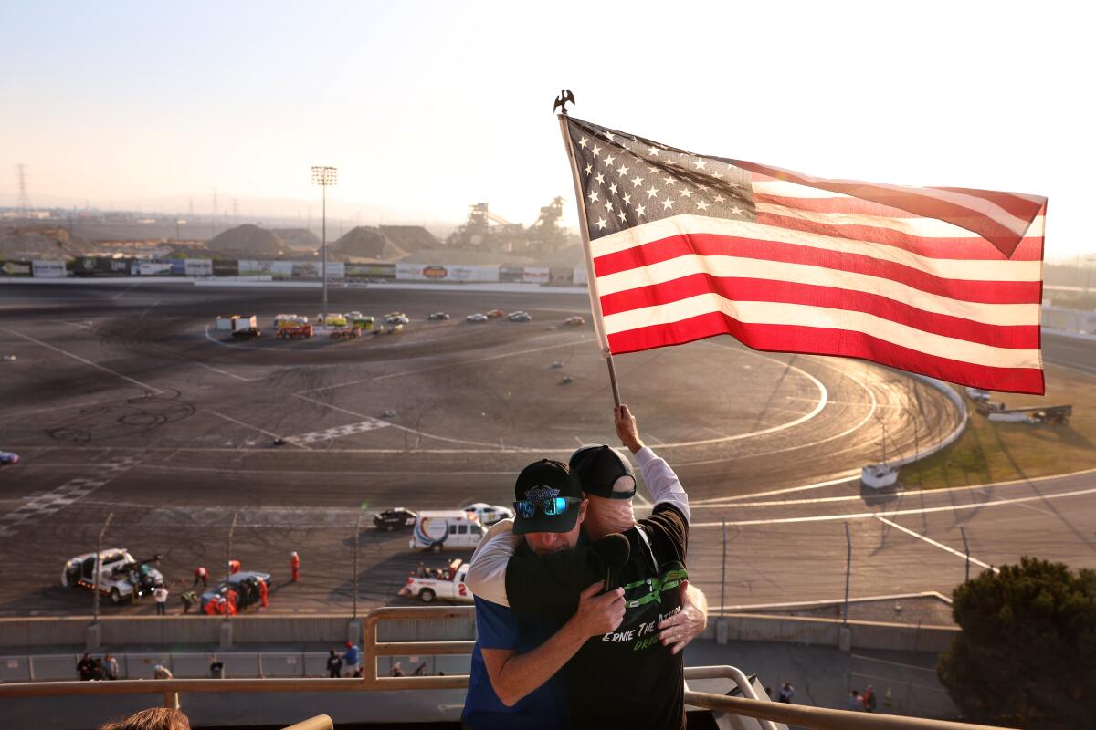 Racing fans embrace while one holds an American flag during the final day of racing at Irwindale Speedway.