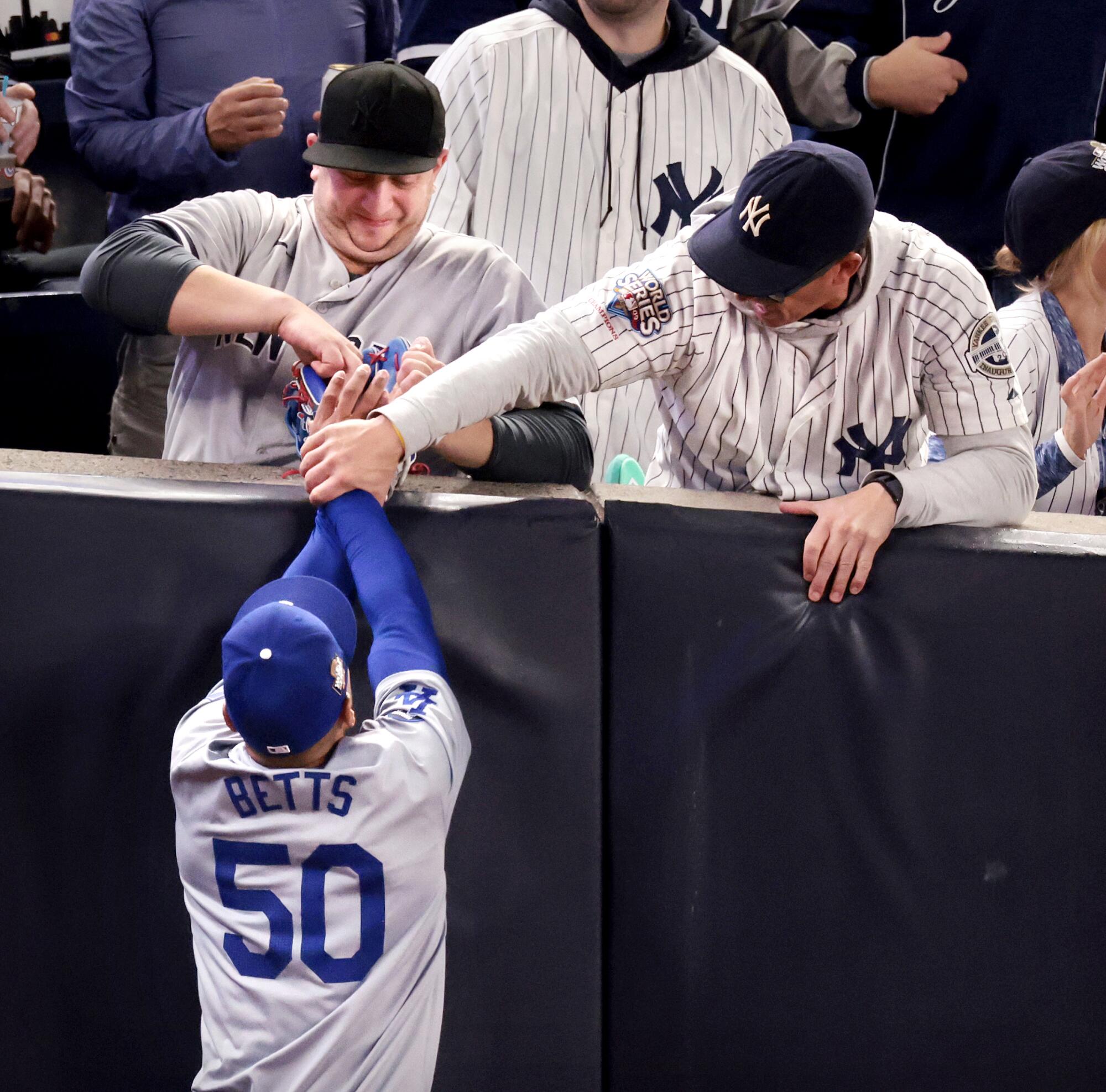 Yankees fans grabs the mitt and arm of Dodgers' Mookie Betts after the right fielder caught the ball in foul territory.